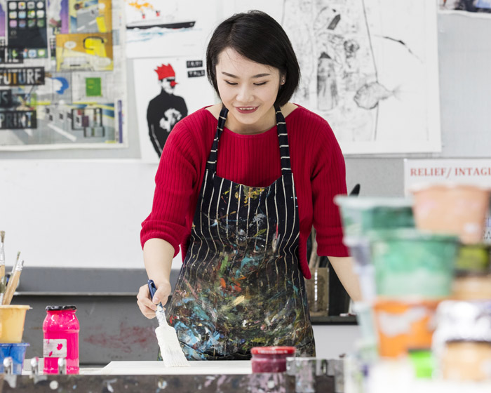 A student in an apron painting in an arts studio