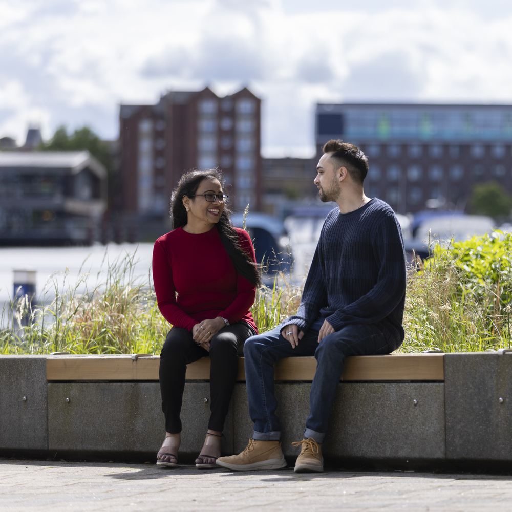Two students socialising on campus in front of the Brayford Pool